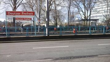 Ein Schild mit der Aufschrift 'Deutzer Freiheit', im Hintergrund eine Brücke und ein Gebäude.