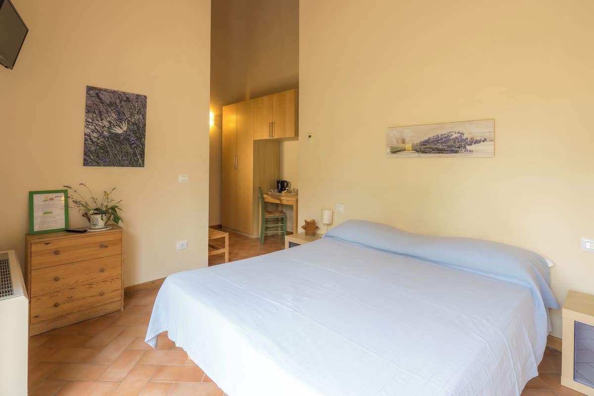 Ein Schlafzimmer mit Bett, Kommode, Schreibtisch und Stuhl. An den Wänden hängen zwei Bilder.