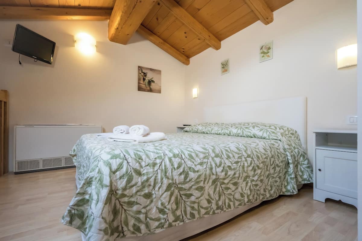 Ein Schlafzimmer mit einem Bett, einem Nachttisch, einem an der Wand befestigten Fernseher und einer Heizung.