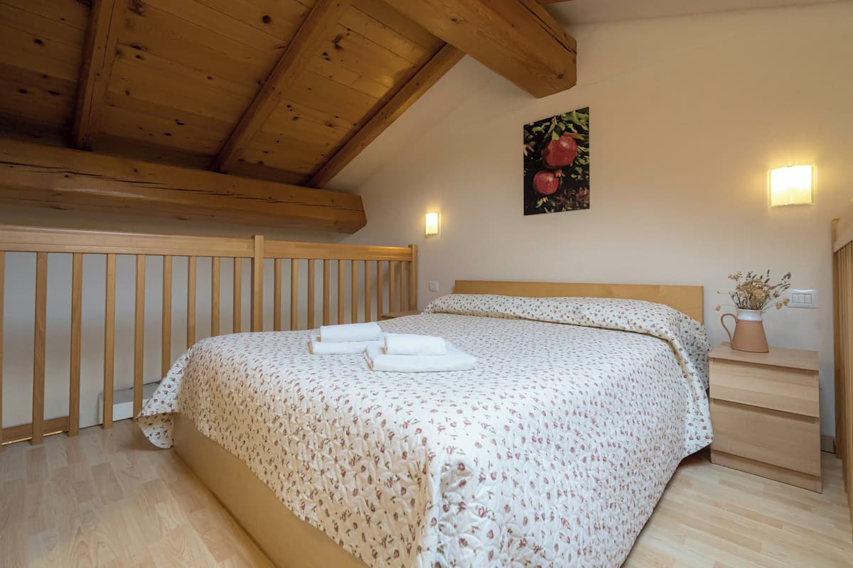 Ein Schlafzimmer mit Holzboden, einem Bett mit floralem Bettbezug, einem Nachttisch mit einer Vase und einer Wandleuchte.