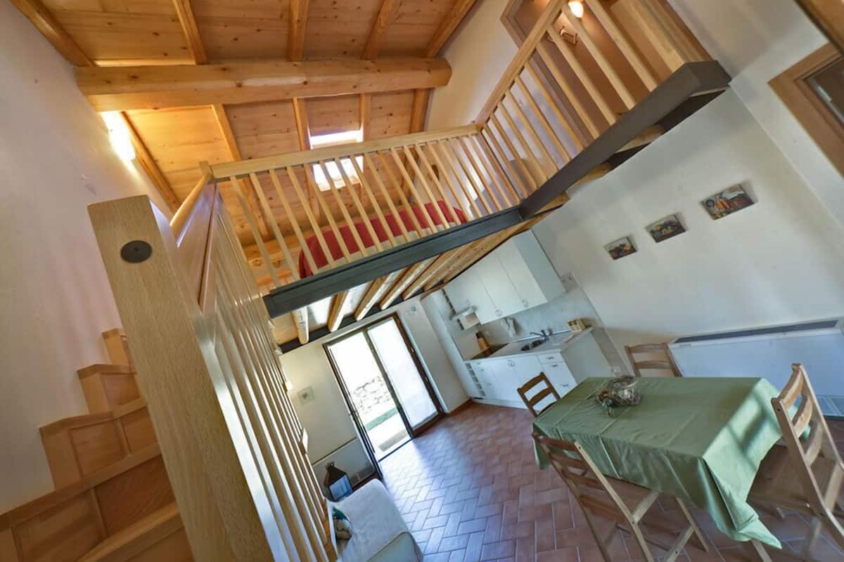 Ein Loft-Zimmer mit einer Holztreppe, einem Essbereich mit Tisch und Stühlen sowie einer Küchenzeile.