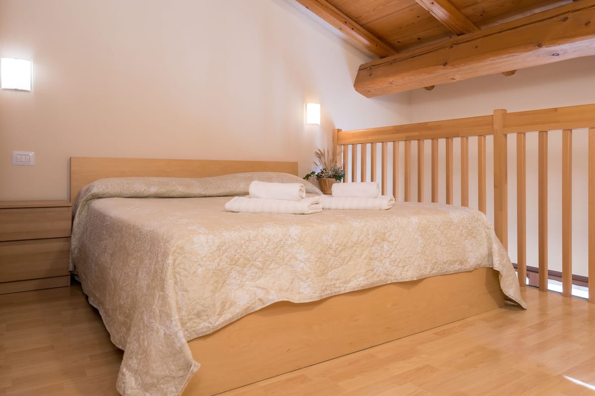 Ein Schlafzimmer mit einem Holzkopfteil, einem Bett mit einer beigen Steudecke und einem Nachttisch mit einer Lampe.