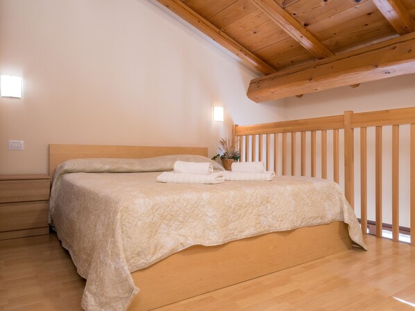 Un dormitorio con cabecera de madera, cama con colcha color beige y mesita de noche con lámpara.