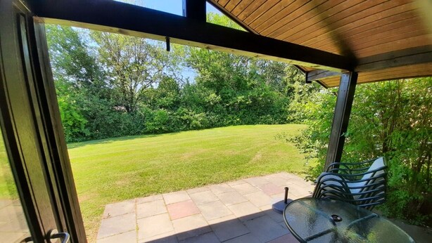 A covered patio with a glass table and chairs, a grassy lawn, and a wooden ceiling. - Holiday park- Robinson (Waldbrunn)