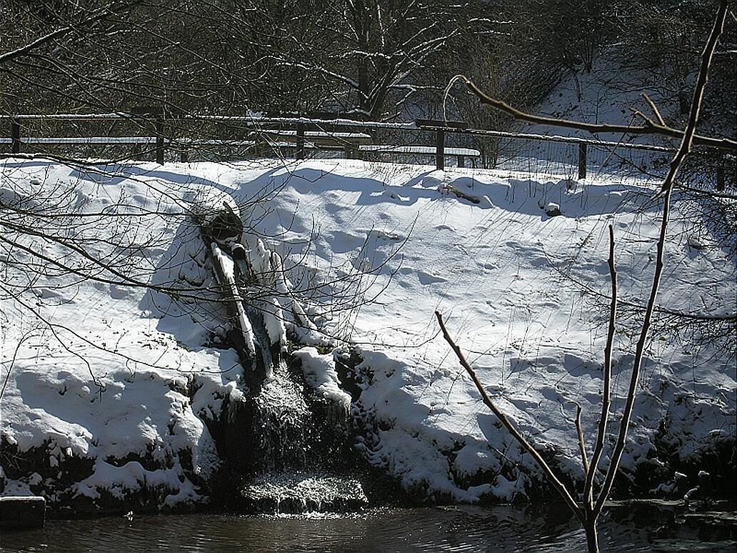 A snow-covered landscape with a frozen river and a wooden bridge.
