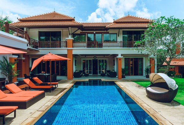 Ein zweistöckiges Haus mit Swimmingpool, Sitzgelegenheiten im Freien und einer überdachten Terrasse.
