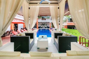 Ein Poolbereich mit Korbmöbeln und Blick auf einen Pool sowie ein Gebäude im Hintergrund.