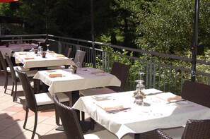 A series of outdoor dining tables with white tablecloths, wicker chairs, and a metal railing. - Restaurant Niedmühle Land & Genuss Hotel (Rehlingen-Siersburg)