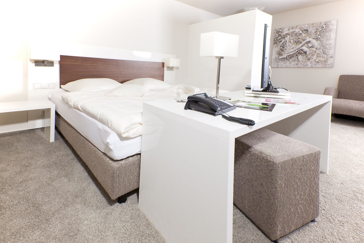 Une chambre d’hôtel avec un lit, un bureau doté d’une lampe, un téléphone et une télécommande.