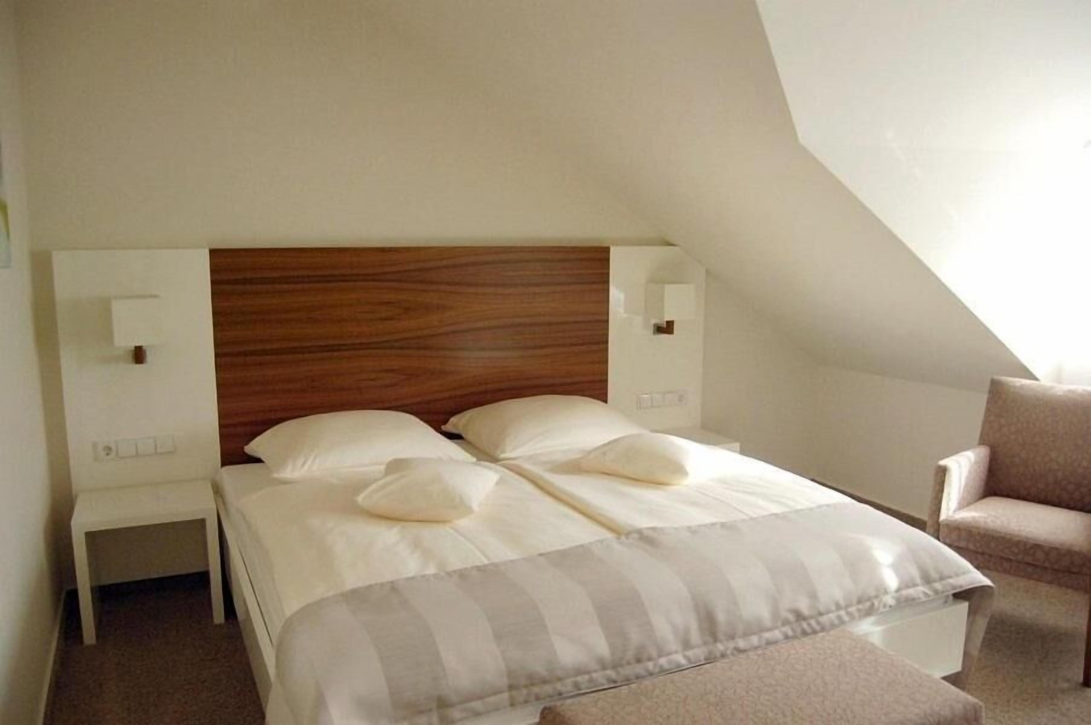 A neatly arranged bedroom with a wooden headboard, two bedside tables, a chair, and a bed with pillows and a striped blanket.