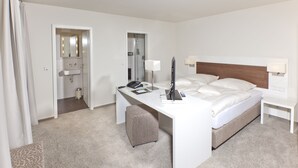A hotel room with a bed, desk, chair, and a bathroom with a sink and mirror. - Restaurant Niedmühle Land & Genuss Hotel (Rehlingen-Siersburg)