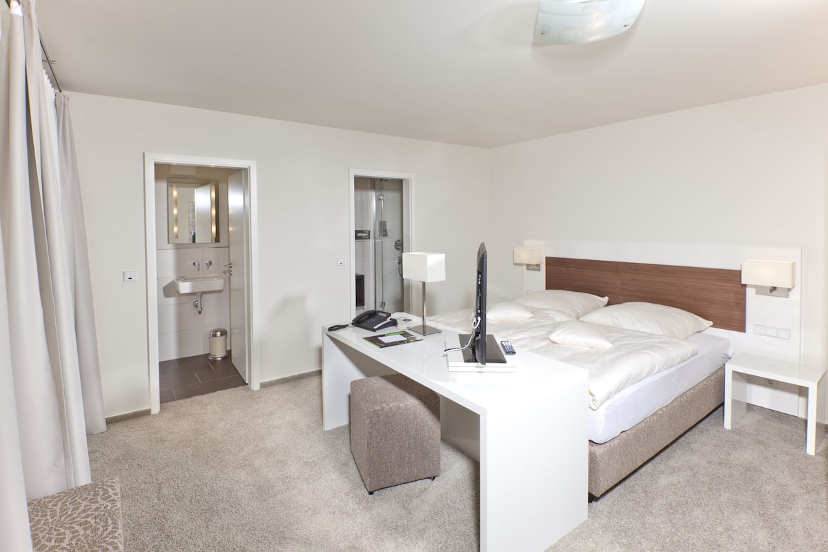 Une chambre d’hôtel comprenant un lit, un bureau, une chaise et une salle de bain avec un lavabo et un miroir.