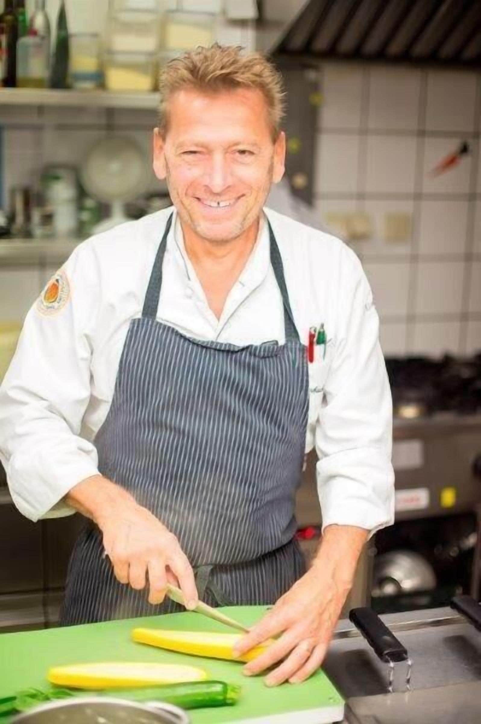 Un chef en una cocina con una tabla de cortar verde, un cuchillo y un vegetal amarillo.