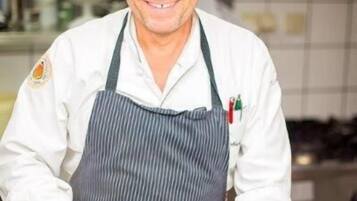 Un chef en una cocina con una tabla de cortar verde, un cuchillo y un vegetal amarillo.