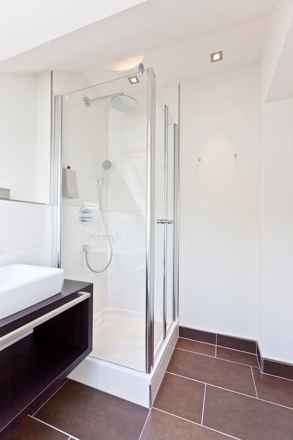 Un baño moderno con ducha de vidrio, azulejos blancos y encimera oscura.