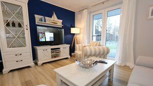 Una sala de estar con televisor, un aparador con puertas de cristal, un sofá a rayas y una mesa de centro.