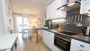 Una cocina moderna con armarios blancos, encimera negra, electrodomésticos de acero inoxidable y un comedor con mesa y sillas.