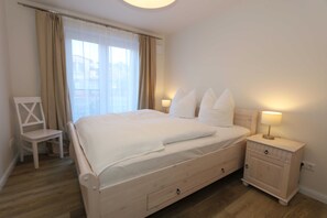 Une chambre à coucher avec un lit, une table de chevet, une chaise et une fenêtre avec des rideaux.