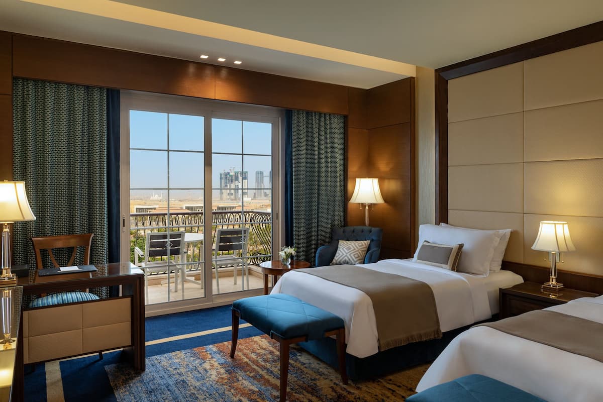 A hotel room with two beds, a balcony with a city view, and a desk with a chair.