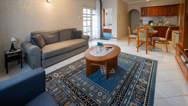 A living room with a sofa, a coffee table, and a patterned rug. There is a dining area with a table and chairs.