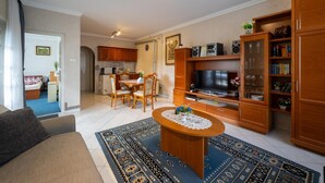 A living room with a sofa, a coffee table, a TV, wooden cabinets, and a dining area with chairs and a table.