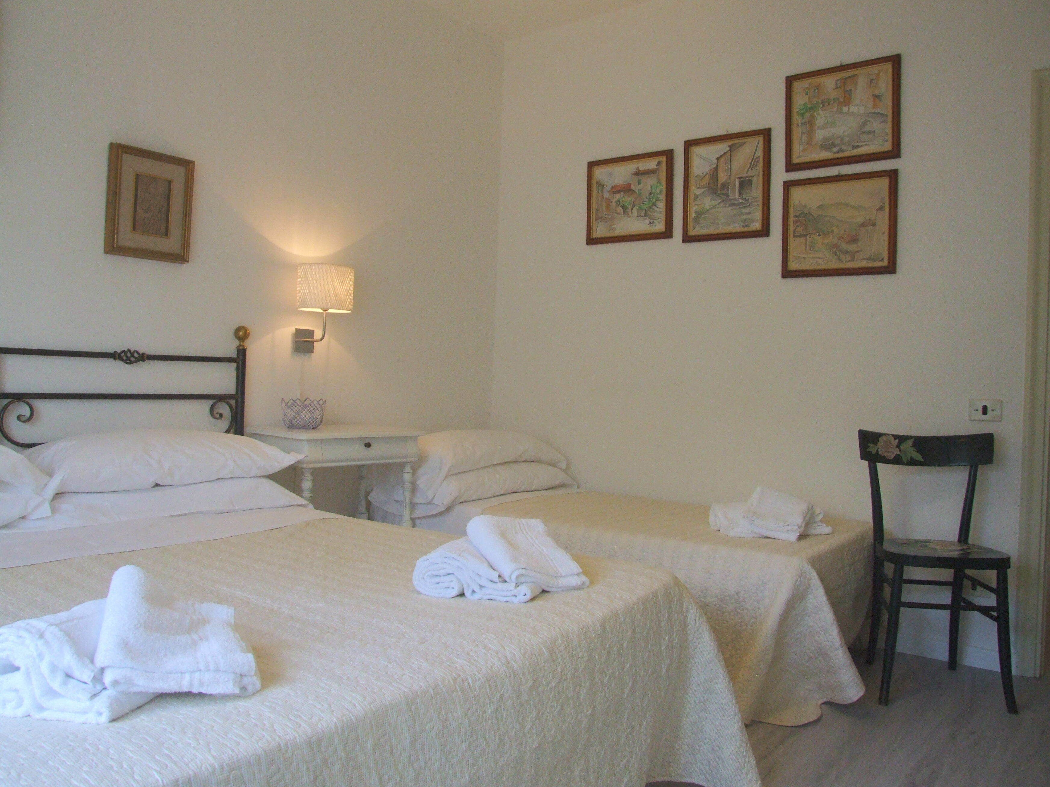 Ein Hotelzimmer mit zwei Betten, einem Nachttisch, einem Sessel und vier gerahmten Bildern an der Wand.