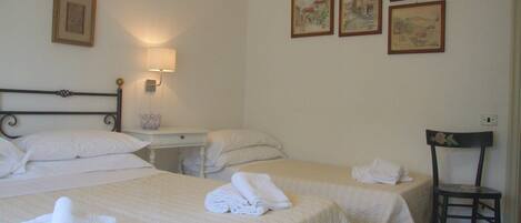 Ein Hotelzimmer mit zwei Betten, einem Nachttisch, einem Sessel und vier gerahmten Bildern an der Wand.