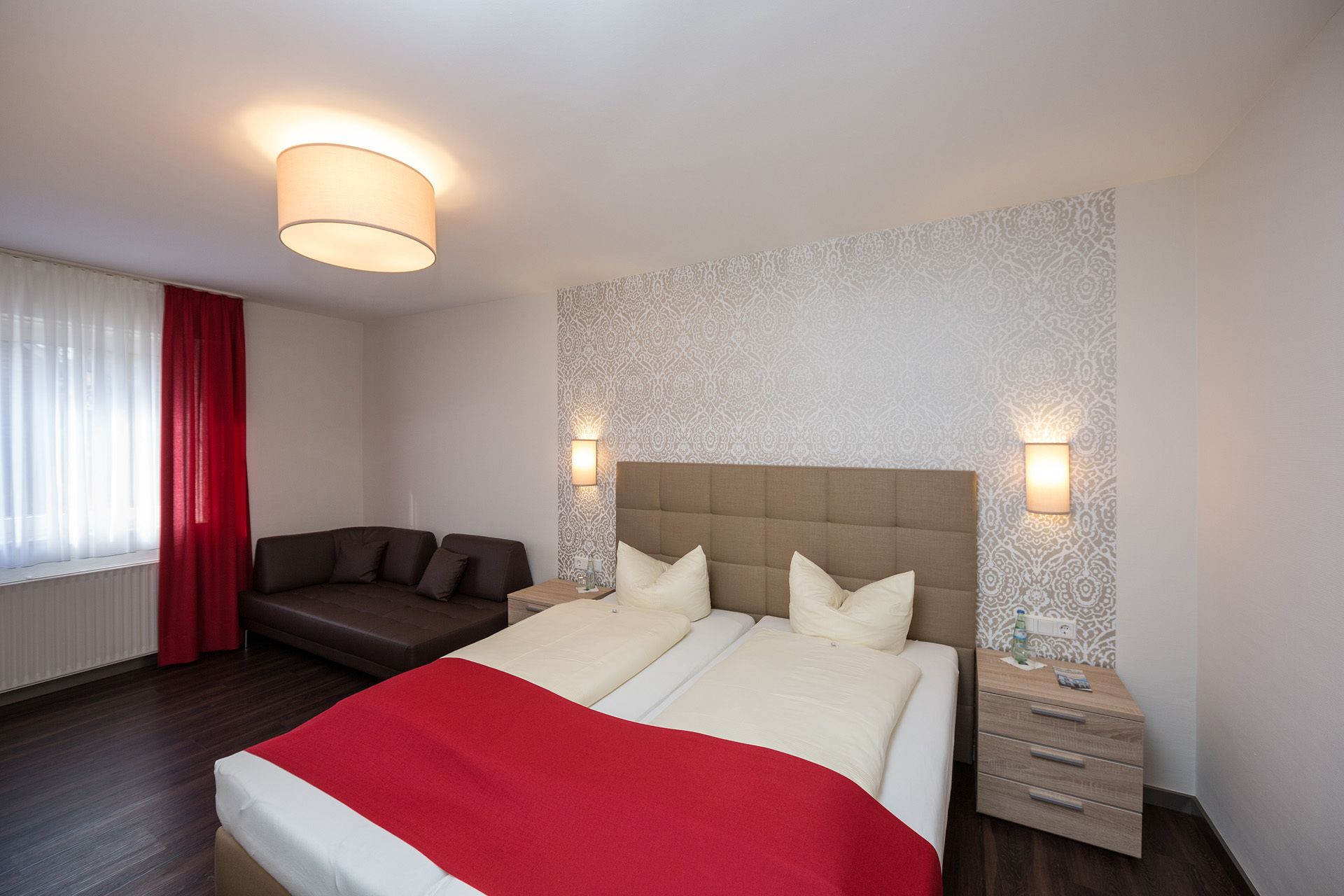 Ein Hotelzimmer mit Bett, Sofa, Nachttisch und einer Wandleuchte.