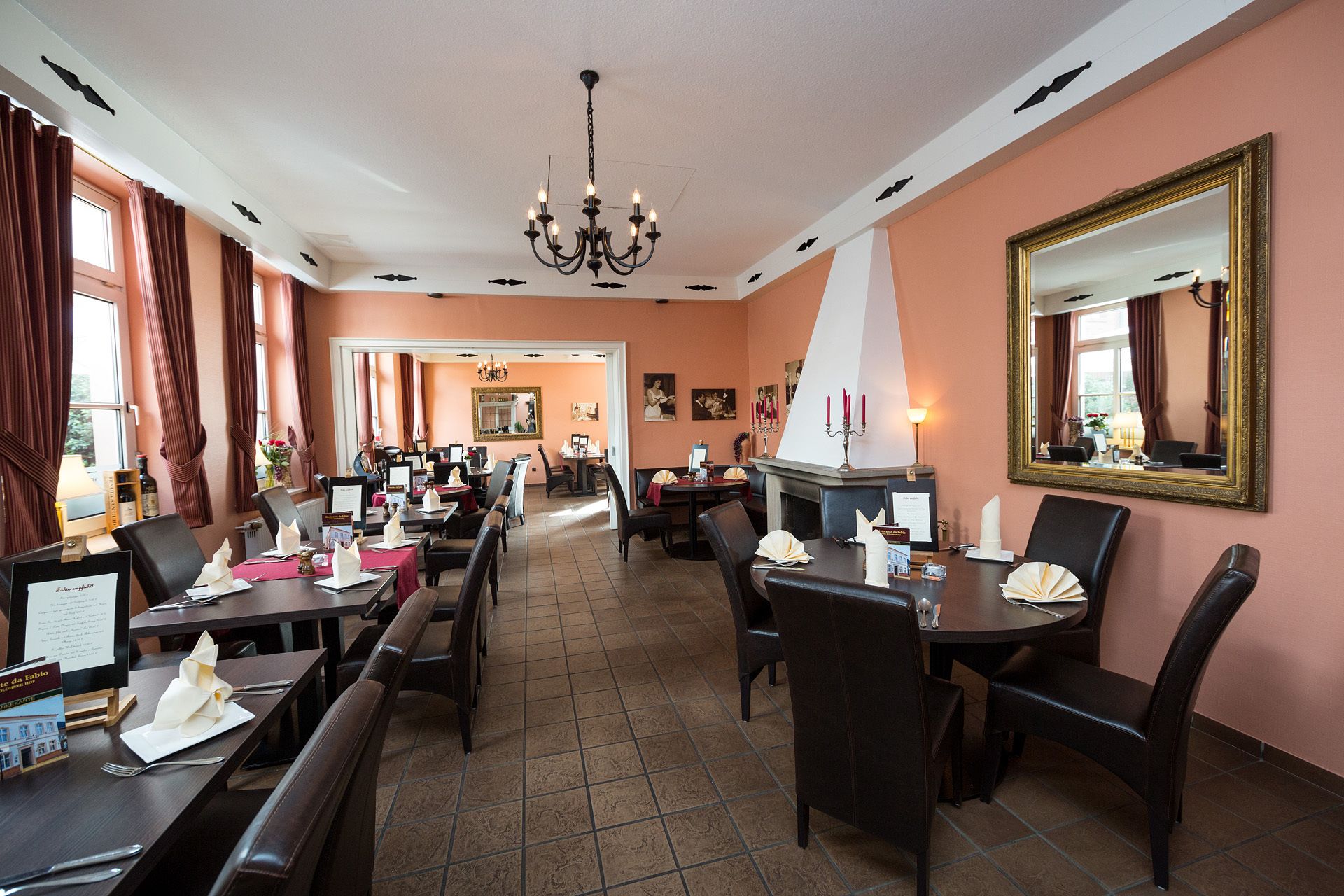 A restaurant with multiple tables and chairs, a chandelier, and a large mirror on the wall.