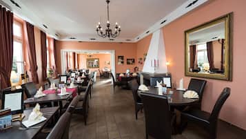 A restaurant with multiple tables and chairs, a chandelier, and a large mirror on the wall.