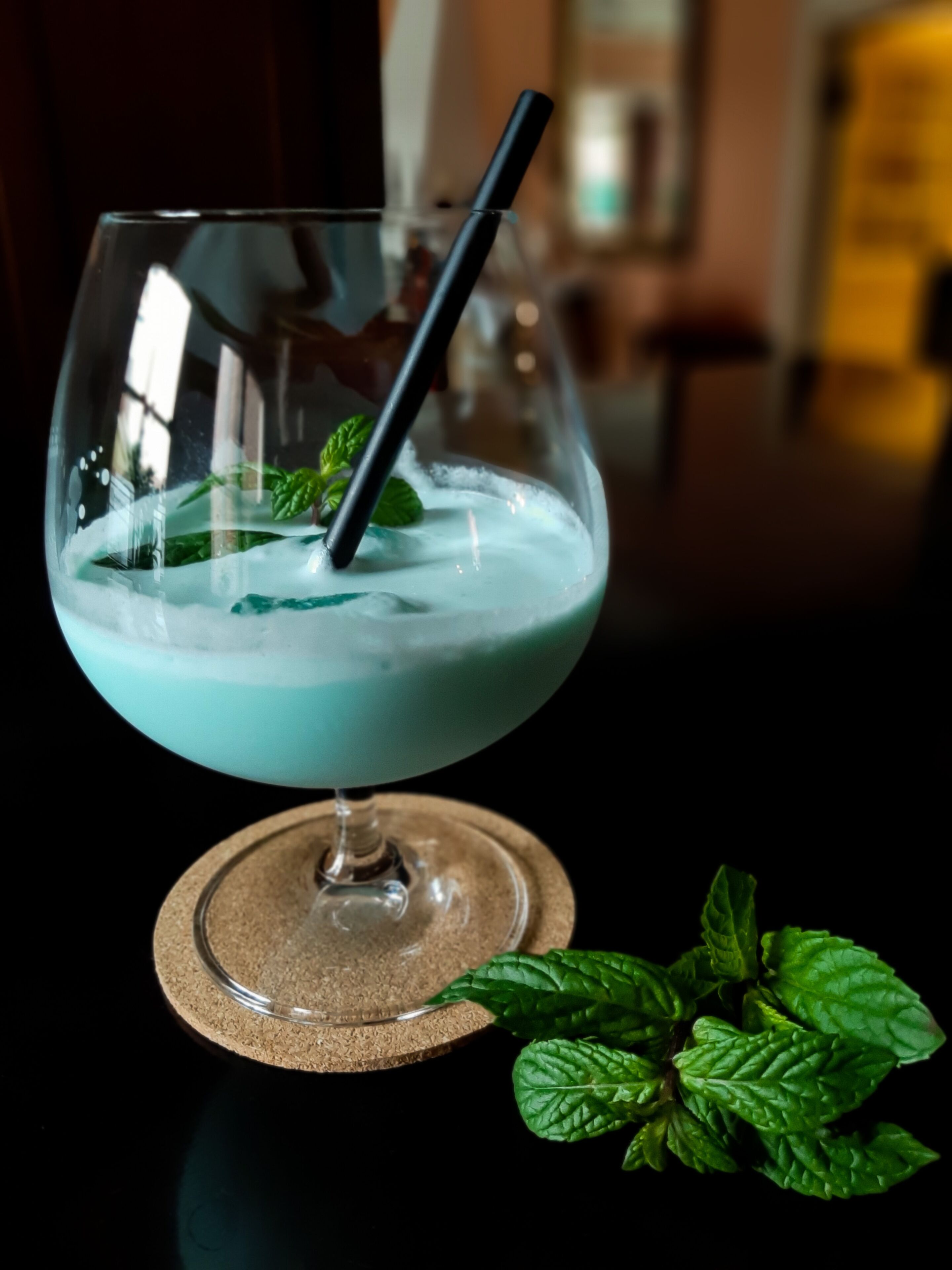 A cocktail in a glass with a straw, garnished with mint leaves, on a coaster.
