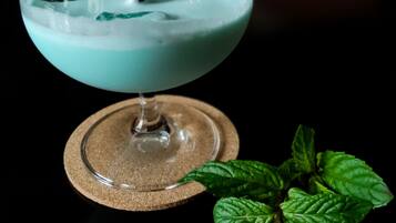 A cocktail in a glass with a straw, garnished with mint leaves, on a coaster.