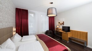 Una habitación de hotel con una cama, un escritorio con ordenador, una silla y un televisor.