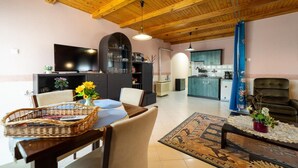 A spacious living area with a dining table, chairs, a TV, kitchen cabinets, and a kitchen in the background. - Cedar  Apartment 3 - One Bedroom Apartment, Sleeps 4 (Zalakaros)