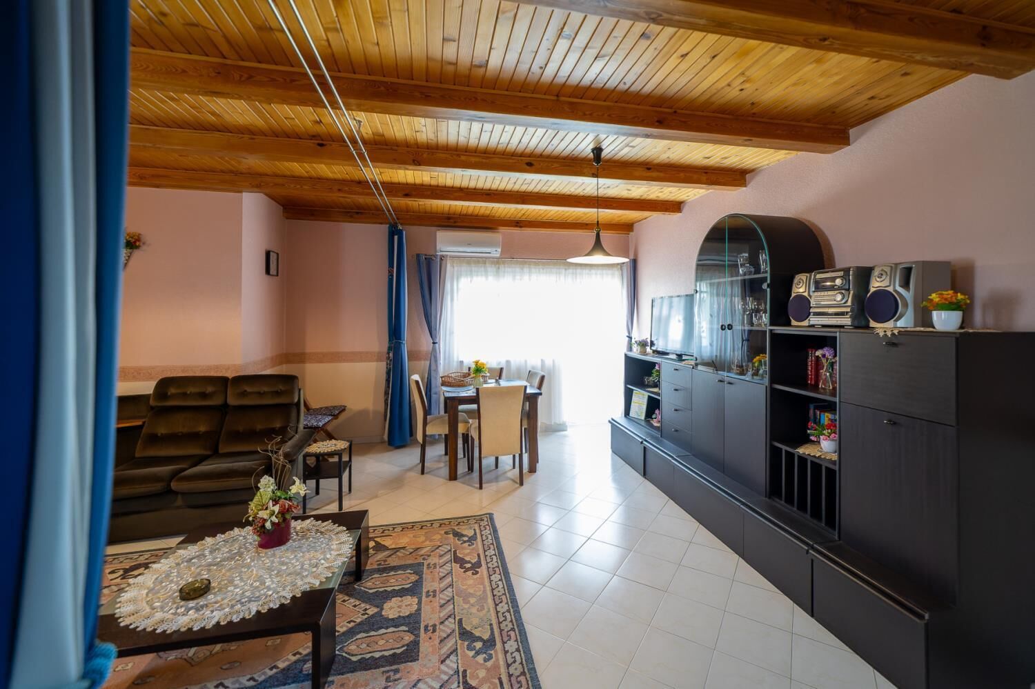 Una sala de estar con techo de madera, un comedor y un mueble de televisión con parlantes.