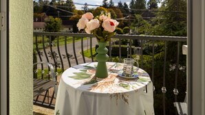 A round table with a floral tablecloth on a balcony, a vase with flowers, and a glass on the table. - Cedar  Apartment 3 - One Bedroom Apartment, Sleeps 4 (Zalakaros)