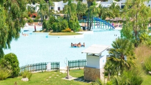 Una piscina rodeada de exuberante vegetación y edificios blancos.
