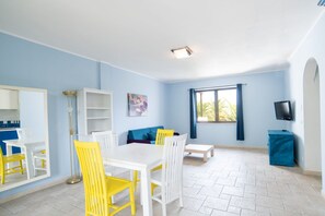 A bright room with a dining table, chairs, a sofa, a TV, and a window with curtains. - Bilocale - One Bedroom Apartment, Sleeps 4 (Castellaneta)