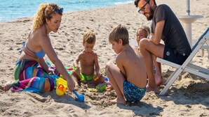 Escena de playa con gente sentada en la arena, algunos jugando con juguetes.