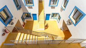 Un immeuble à plusieurs étages, doté d’un escalier central, de fenêtres à cadre bleu et d’un plancher jaune.