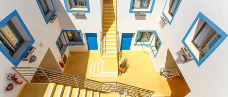 Un edificio de varios niveles con una escalera central, ventanas de marco azul y piso amarillo.