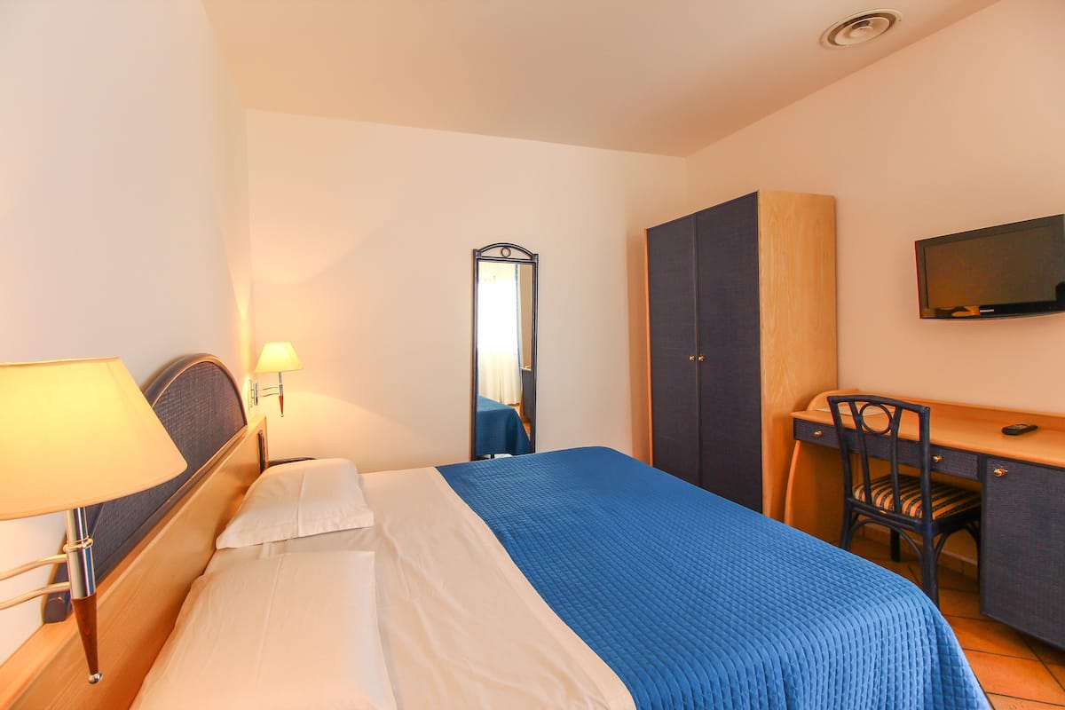 Una habitación de hotel con una cama, un escritorio, una silla, un espejo y una televisión.