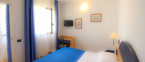 A hotel room with a bed, a desk, a chair, a TV, and a lamp.