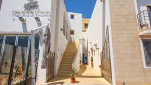 L’entrée d’un hôtel, avec un escalier menant aux étages supérieurs, une enseigne indiquant « Paladini di Francia » et un ciel bleu azur au-dessus.