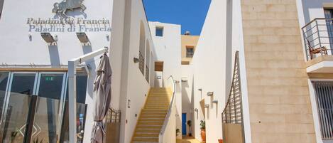 Entrada de un hotel con una escalera que lleva a los pisos superiores, un letrero que dice "Paladini di Francia" y un cielo azul despejado.