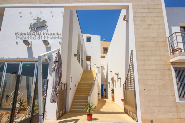 A hotel entrance with a staircase leading to the upper floors, a sign reading "Paladini di Francia," and a clear blue sky above.
