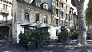 A building with a cafe named 'LE CAFE DU COLLONCES' on the ground floor, surrounded by potted plants and a tree. - Hôtel Le Collonges (Brive-la-Gaillarde)