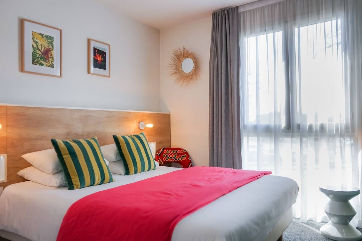 A hotel room with a bed, a round mirror, and two framed pictures on the wall.