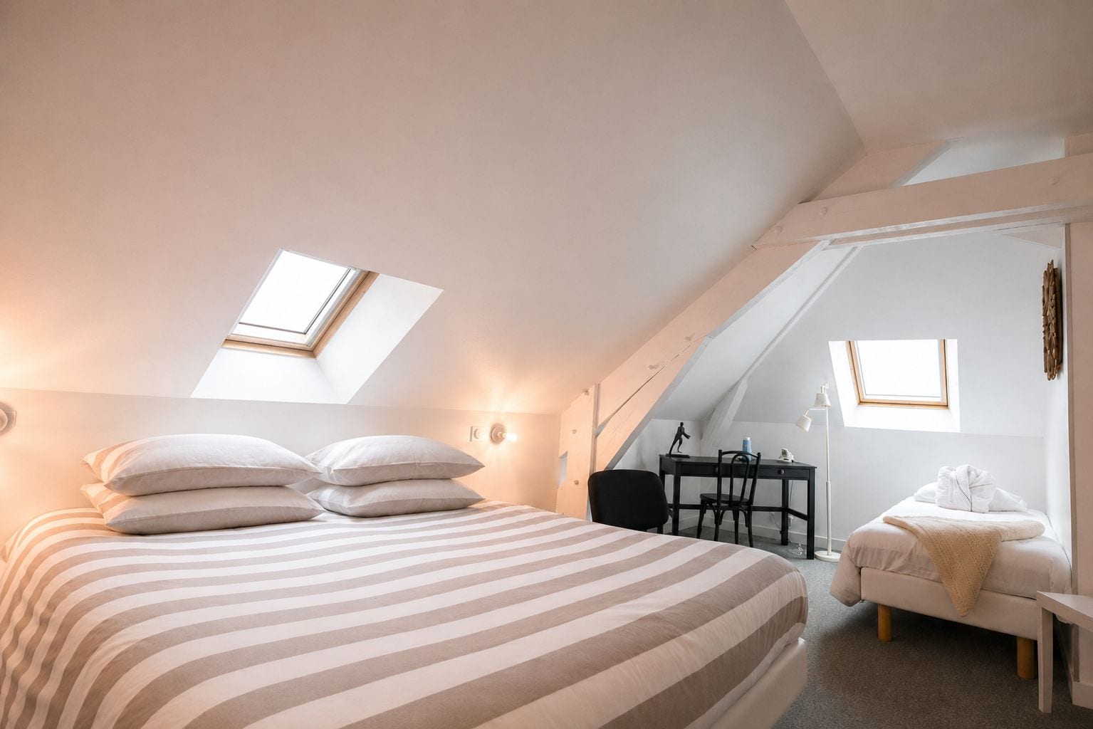 Une chambre à coucher avec un lit, un bureau et une chaise. Il y a des fenêtres de toit au plafond.