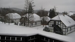 Una hilera de edificios modernos cubiertos de nieve, con grandes ventanales y techos planos, rodeados de árboles y un paisaje montañoso al fondo.